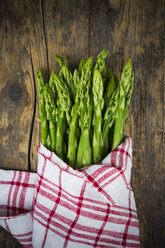 Bündel grüner Spargel, Asparagus officinalis, eingewickelt in ein Küchentuch, auf dunklem Holz liegend - LV001448