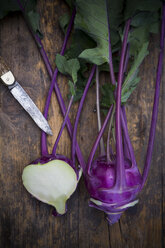 Whole and a half blue turnip cabbages, Brassica oleracea var. gongylodes L. and a knife on dark wood, elevated view - LVF001458