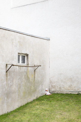 Deutschland, trüber Hinterhof mit Puppe, die in einer Ecke im Gras sitzt, lizenzfreies Stockfoto