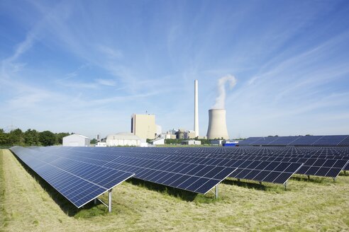 Germany, North Rhine-Westphalia, Petershagen-Lahde, Field with solar panels and a coal-fired power station in the background - HAWF000327