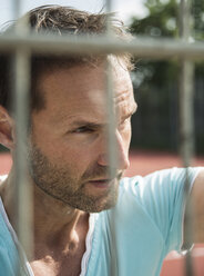 Germany, Mannheim, Man on sports field looking through fence - UUF001104