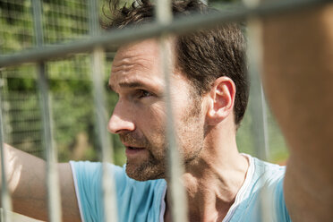 Germany, Mannheim, Man on sports field looking through fence - UUF001105