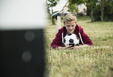 Germany, Mannheim, Teenage boy with soccer ball, using smartphone - UUF001155