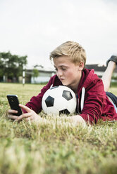 Deutschland, Mannheim, Jugendlicher mit Fußball, mit Smartphone - UUF001156