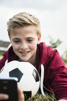Deutschland, Mannheim, Jugendlicher mit Fußball, mit Smartphone - UUF001157