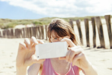 Porträt einer Frau, die mit ihrem Smartphone am Strand fotografiert - MFF001135