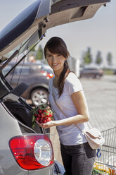 Porträt einer lächelnden jungen Frau, die einen Einkauf in ihr Auto lädt - GDF000337