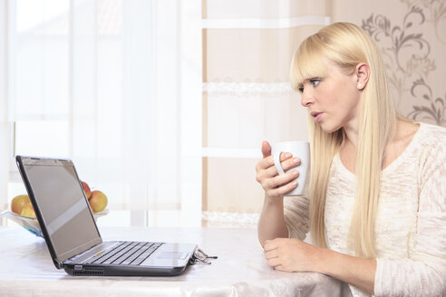 Porträt einer jungen Frau mit einer Tasse und einem Laptop zu Hause - VTF000308