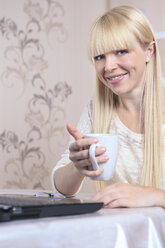 Portrait of smiling young woman with a cup and a laptop at home - VTF000305