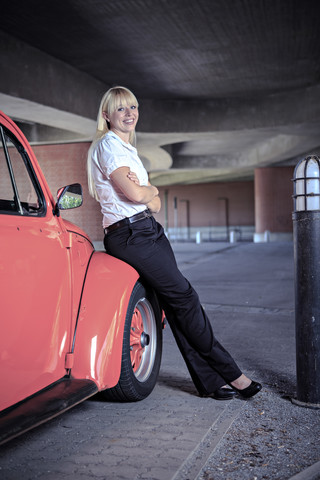 Portrait of a smiling young woman sitting on car wing of a classic car stock photo