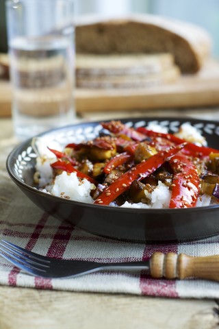 Süß-saure Aubergine mit rotem Pfeffer auf Reis und garniert mit Sesamsamen, lizenzfreies Stockfoto