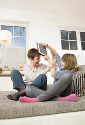 Germany, Berlin, Mother and daughter play fighting on sofa - MMFF000031