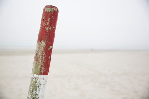 Deutschland, Niedersachsen, Ostfriesland, Langeoog, rot-weißer Holzpfahl vor dem Strand - JATF000744