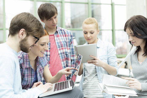 Studenten in einer Universitätsbibliothek mit digitalem Tablet und Laptop, lizenzfreies Stockfoto