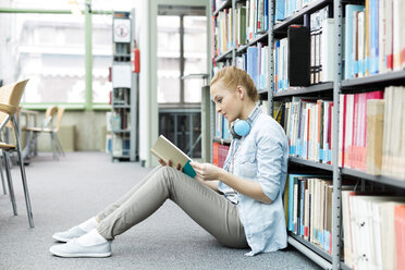 Student in einer Universitätsbibliothek sitzt auf dem Boden und liest ein Buch - WESTF019574