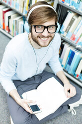 Student in einer Universitätsbibliothek, der mit Kopfhörern auf dem Boden sitzt - WESTF019578