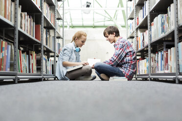 Zwei Studenten in einer Universitätsbibliothek sitzen auf dem Boden und lesen Bücher - WESTF019618