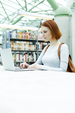 Student in einer Universitätsbibliothek mit Laptop, lizenzfreies Stockfoto