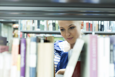 Student in einer Universitätsbibliothek, der ein Buch im Regal liest - WESTF019669