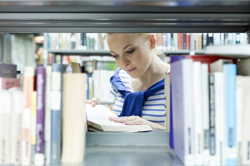 Student in einer Universitätsbibliothek, der ein Buch im Regal liest - WESTF019670