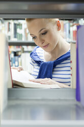 Student in einer Universitätsbibliothek, der ein Buch im Regal liest - WESTF019671