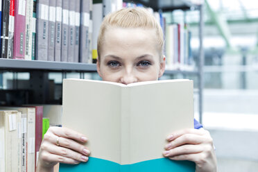 Student in a university library holding book - WESTF019580