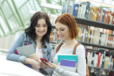 Zwei Studenten in einer Universitätsbibliothek mit Mobiltelefon - WESTF019733