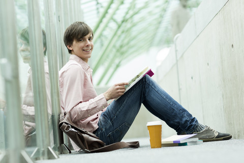 Student in einer Universitätsbibliothek sitzt auf dem Boden und liest ein Buch, lizenzfreies Stockfoto