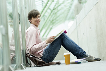 Student in einer Universitätsbibliothek sitzt auf dem Boden und liest ein Buch - WESTF019738