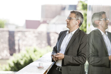 Businessman listening to music on balcony - DISF000862