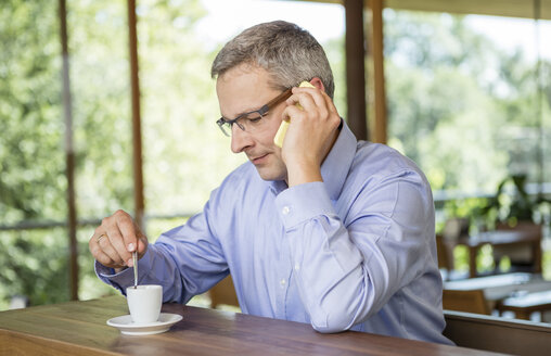 Geschäftsmann in einem Café, der ein Mobiltelefon benutzt - DISF000869