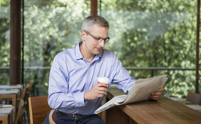 Businesman reading newspaper in cafe - DISF000871