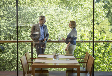 Geschäftsmann und Geschäftsfrau unterhalten sich auf einem Balkon vor einem Restaurant - DISF000874