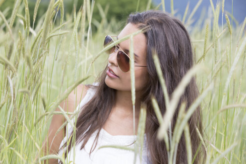 Porträt einer jungen Frau mit Sonnenbrille in einem Feld sitzend - DRF000703