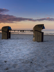 Germany, Schleswig-Holstein, Scharbeutz, Sea bridge, Roofed wicker beach chairs at beach in the evening - AMF002464