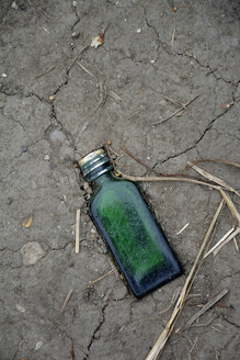 Green glass bottle trodden in soil, elevated view - AX000708