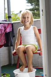Portrait of little girl taking foot bath on balcony - JFEF000437