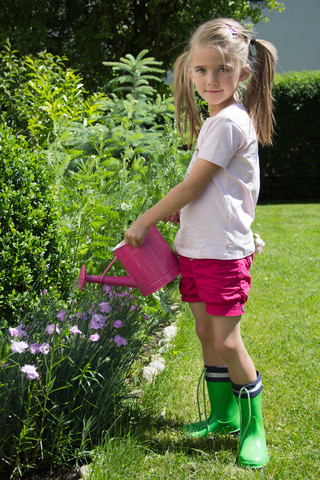 Porträt eines kleinen Mädchens, das mit einer rosa Gießkanne im Garten Pflanzen gießt, lizenzfreies Stockfoto