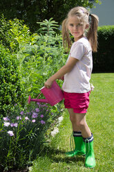 Porträt eines kleinen Mädchens, das mit einer rosa Gießkanne im Garten Pflanzen gießt - YFF000188