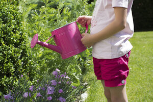 Kleines Mädchen gießt Pflanzen mit rosa Gießkanne im Garten, Teilansicht - YFF000187