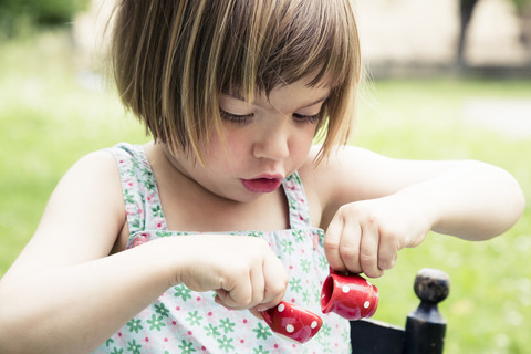 Porträt eines kleinen Mädchens, das mit einem Puppengeschirr im Garten spielt, lizenzfreies Stockfoto