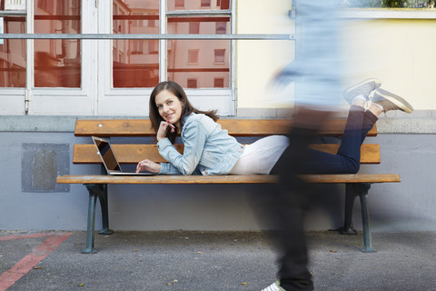 Frau mit Laptop auf Bank liegend mit Passantin, lizenzfreies Stockfoto