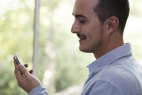 Lächelnder Mann schaut auf sein Handy, lizenzfreies Stockfoto