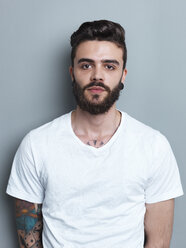 Portrait of tattooed brunette man in front of gray background - STKF000953