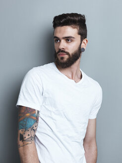 Portrait of tattooed brunette man in front of gray background - STKF000954
