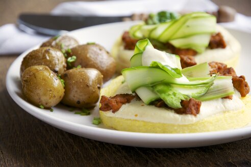 Polenta mit veganer Käsesauce, würzigen Tofustücken und Spargel, serviert mit gekochten Babykartoffeln - HAWF000356