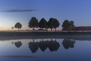 Deutschland, Niedersachsen, Gifhorn, See und Spiegelungen von Bäumen, Straße mit Lichtspur am Abend - PVCF000025