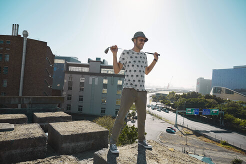 Young man with golf club looking over city, smiling - KOF000001