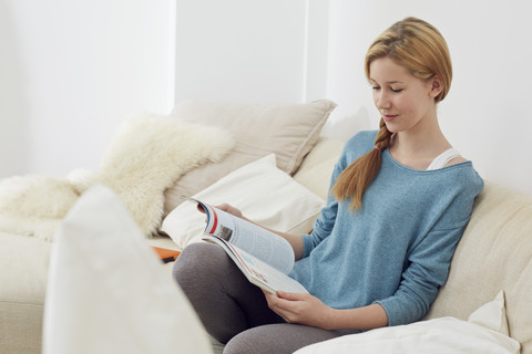 Weiblicher Teenager beim Lesen einer Zeitschrift im Wohnzimmer, lizenzfreies Stockfoto