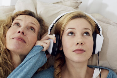 Portrait of mother and daughter listening music with headphones at home - STKF001020